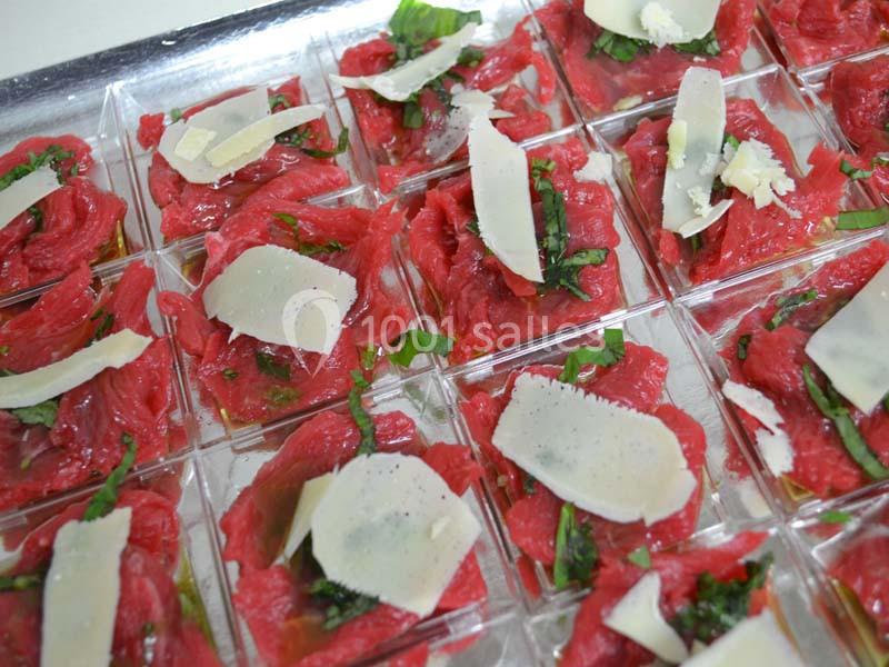 Tranches de carpaccio de bœuf garnies de parmesan, basilic et assaisonnement, présentées dans des verrines individuelles.