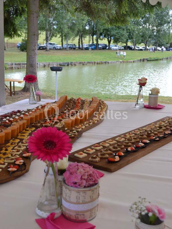 Buffet en plein air avec amuse-bouches variés disposés sur des plateaux en bois près d'un étang entouré d'arbres.