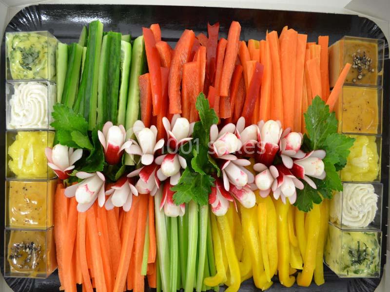 Plateau de crudités colorées avec carottes, concombres, poivrons, radis décoratifs et sauces en accompagnement.