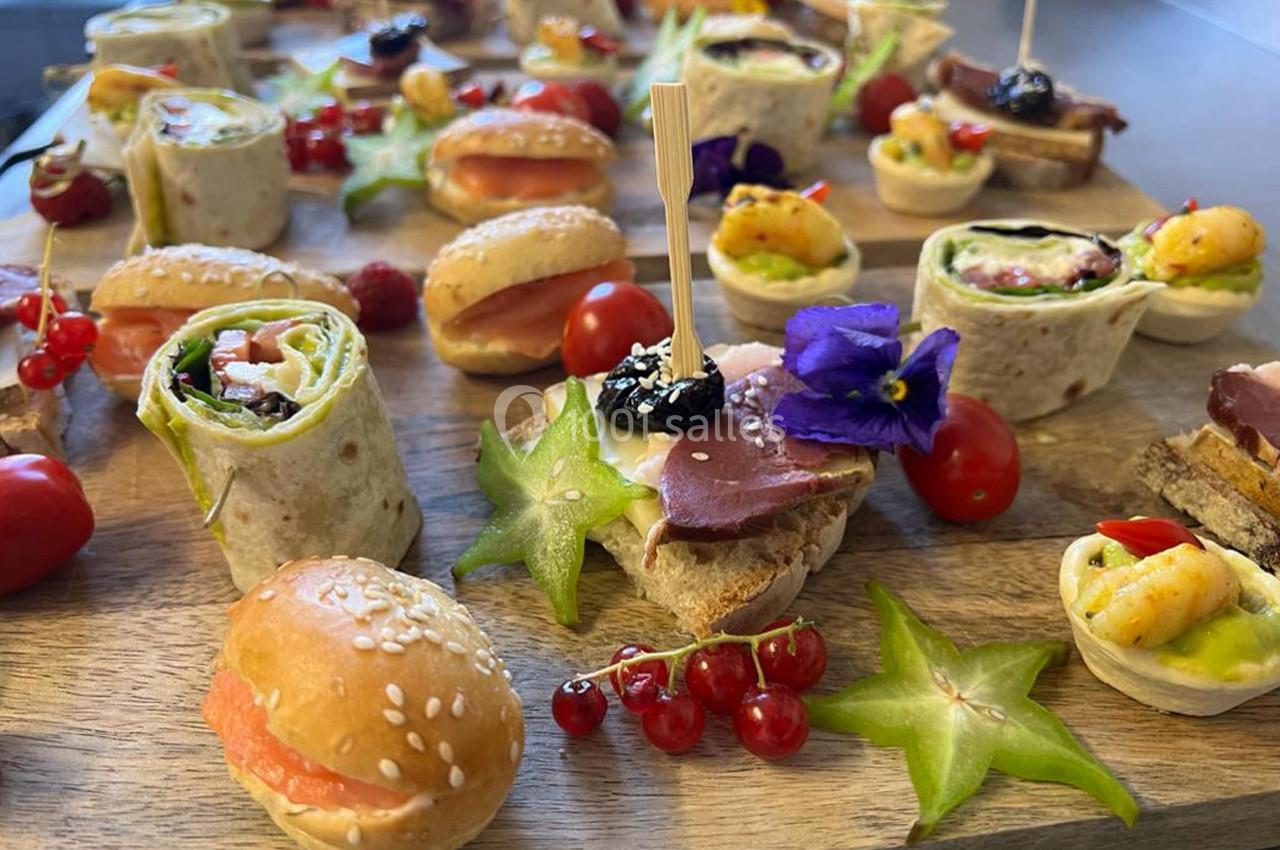 Plateau de bouchées variées comprenant wraps, mini-sandwichs, fruits et garnitures colorées sur une planche en bois.