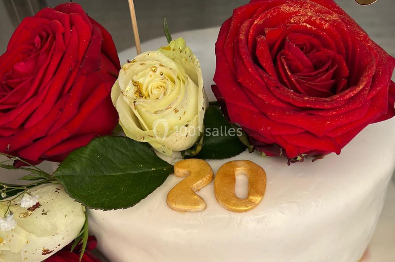 Gâteau décoré de roses rouges et blanches, avec le chiffre ’20’ doré posé sur le glaçage blanc.