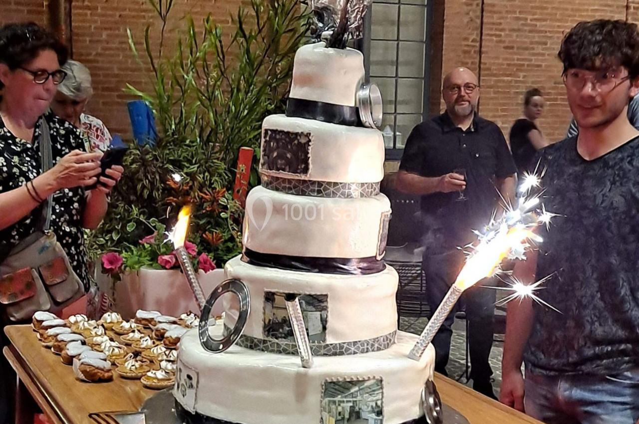 Gâteau de mariage à plusieurs étages décoré de photos et d'étincelles, entouré de desserts et de convives.