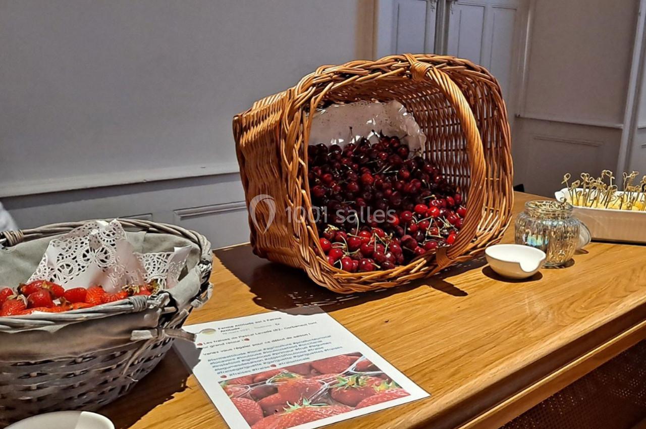 Un panier en osier renversé rempli de cerises sur une table en bois, à côté de fraises et d'autres éléments de présentation.