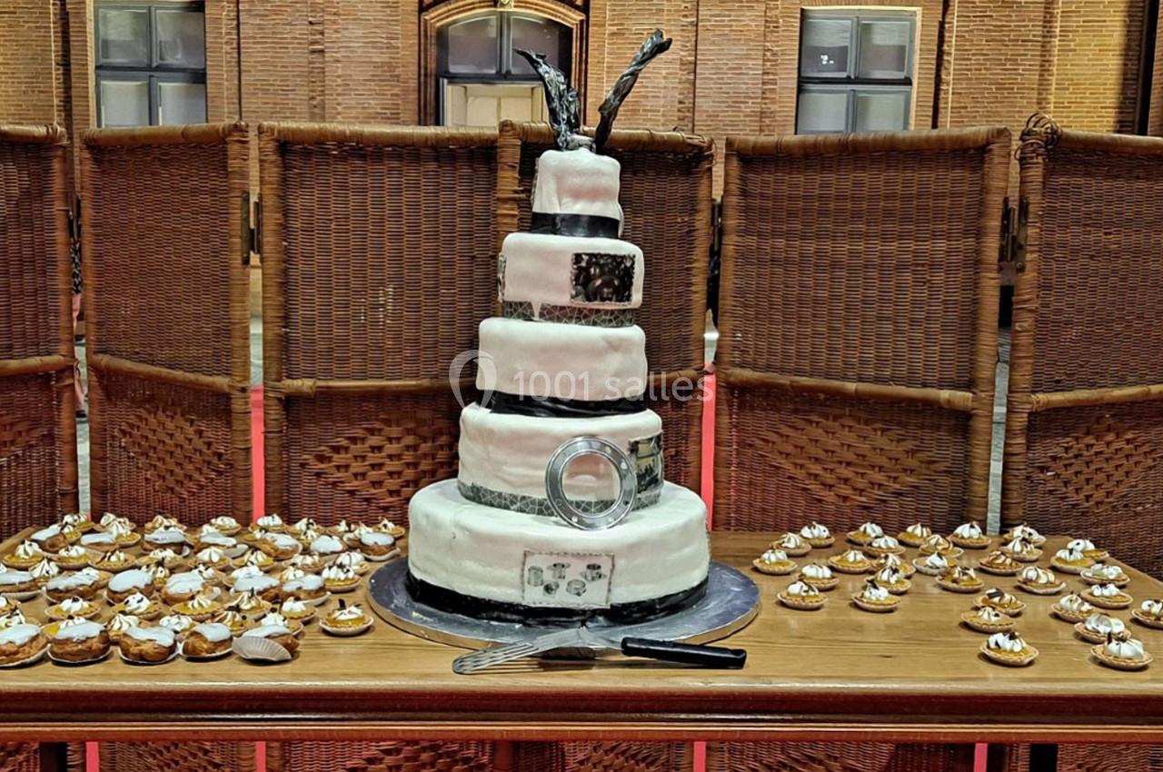 Gâteau de mariage à plusieurs étages décoré de noir et blanc, entouré de petites pâtisseries sur une table en bois.