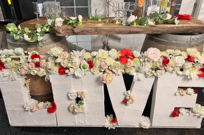 Décoration d'une tente événementielle avec tables ornées, barils en bois, fleurs et ballons dans un espace extérieur.