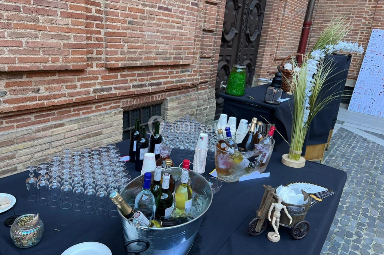Table de réception en extérieur avec boissons, verres, seau à glace et décoration sur fond de mur en briques.