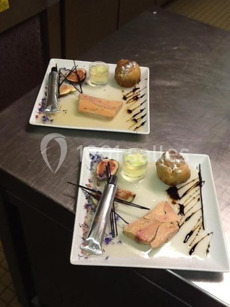 Assiettes dressées avec foie gras, figues, pain, gelée et décorations de sauce sur une table en inox.