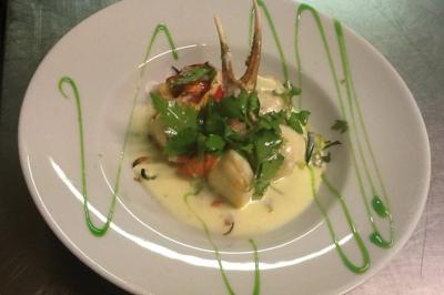 Assiette de poisson en sauce blanche, garnie de persil frais, légumes et décorée de traits de sauce verte.