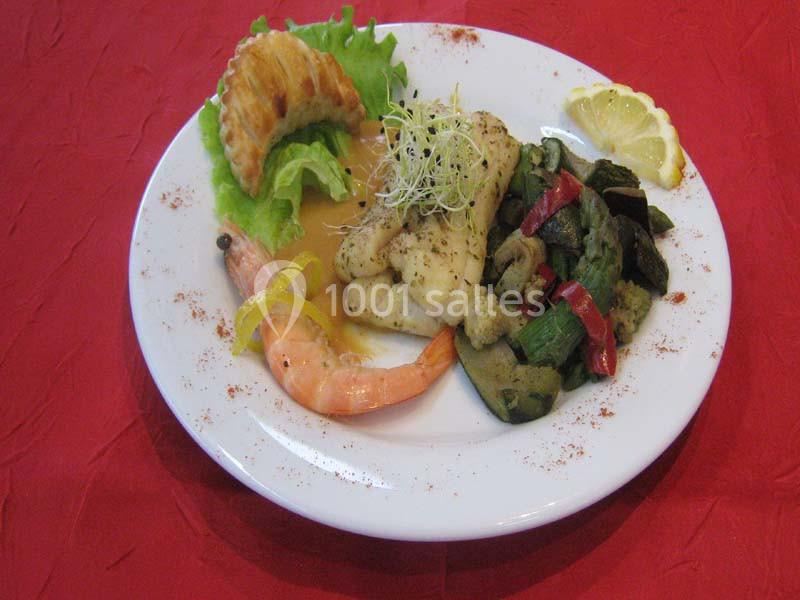 Assiette composée de poisson, crevette, légumes sautés, salade et tranche de citron, présentée sur une nappe rouge.