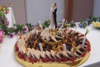 Pyramide de macarons colorés surmontée de figurines de mariés, présentée sur une table rouge en extérieur.