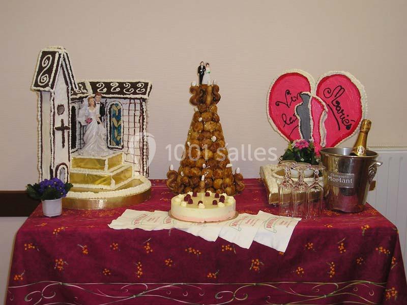 Pièce montée avec croquembouche, décorations de mariage en sucre, champagne et accessoires sur une table rouge.