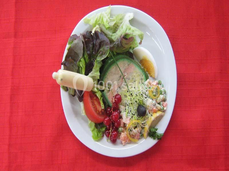 Assiette composée de salade, tomate, œuf, terrine, crudités, groseilles et sauce, présentée sur une nappe rouge.
