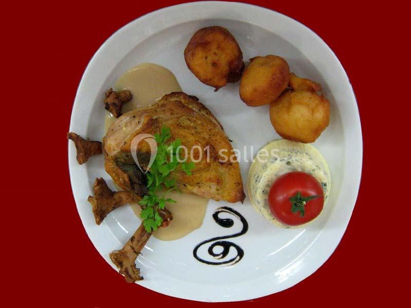 Assiette avec un morceau de volaille, sauce, pommes dauphines, flan salé et tomate décorative sur fond rouge.