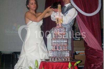 Pyramide de macarons colorés surmontée de figurines de mariés, présentée sur une table rouge en extérieur.