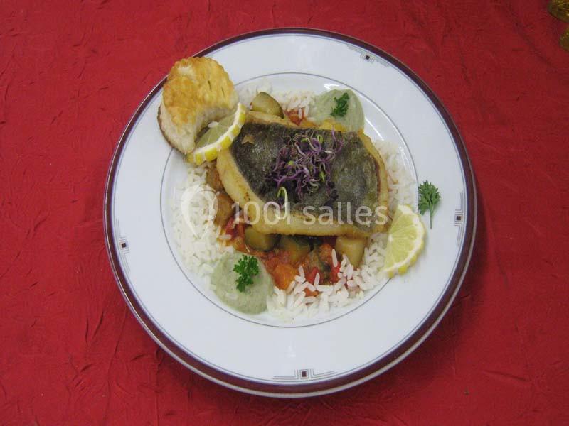 Assiette de poisson grillé sur lit de riz, accompagnée de légumes, citron et herbes, servie sur une nappe rouge.