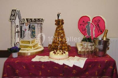 Pyramide de macarons colorés surmontée de figurines de mariés, présentée sur une table rouge en extérieur.