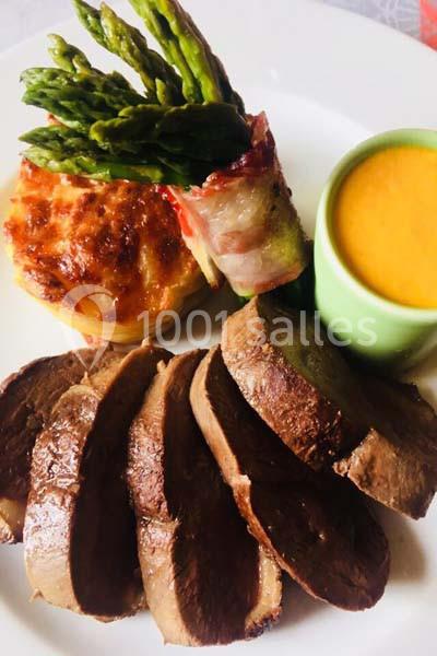 Assiette composée de tranches de viande, gratin de pommes de terre, asperges enroulées de bacon et sauce en accompagnement.