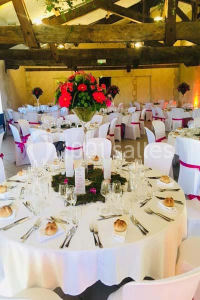 Salle de réception décorée avec des tables rondes, nappes blanches, centres de table fleuris et chaises habillées.