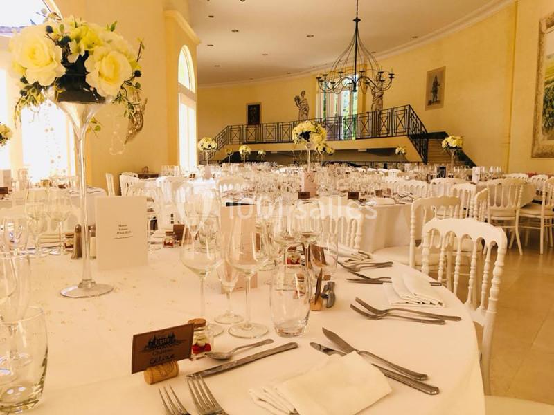 Salle de réception élégamment décorée avec des tables dressées, des fleurs blanches et des chaises blanches.
