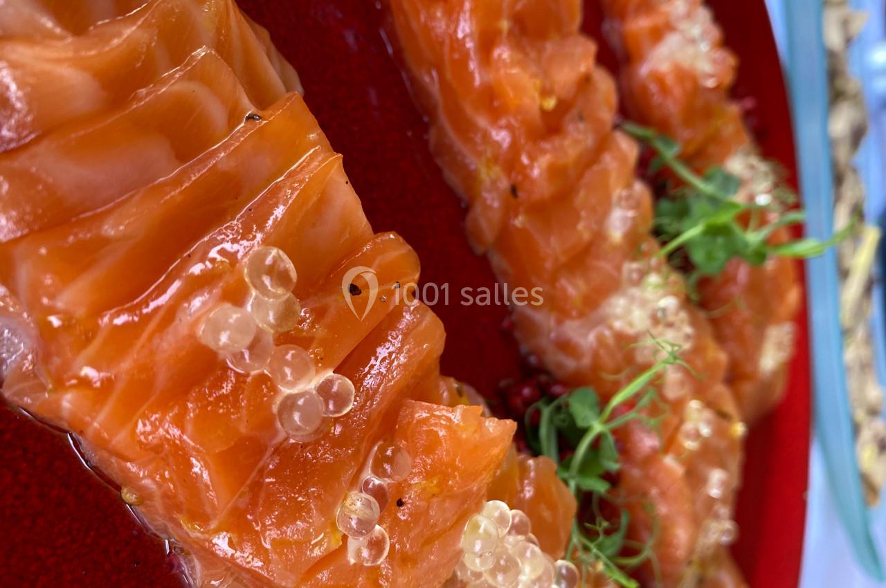 Tranches de saumon cru garnies de perles de citron et de micro-pousses, présentées sur un plat rouge.