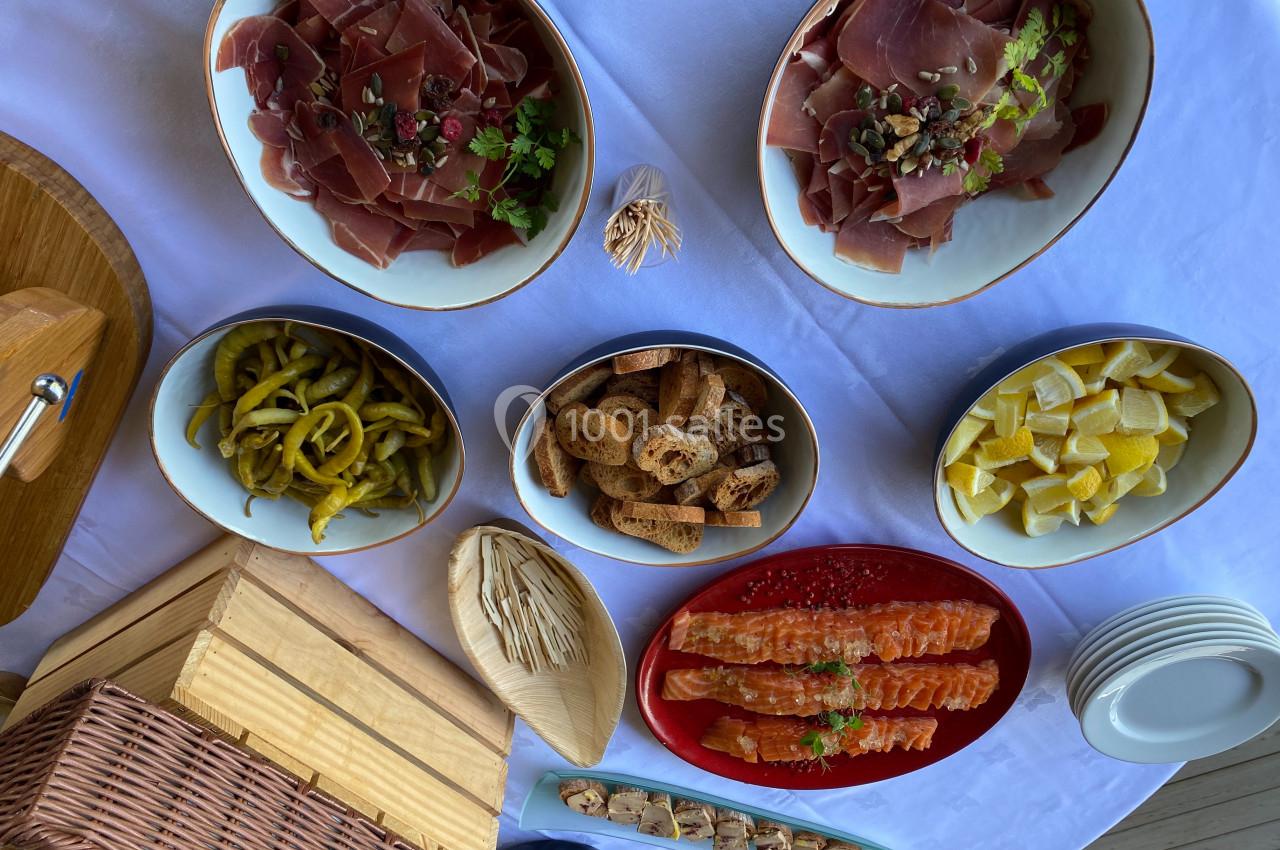 Plateau de buffet avec charcuterie, saumon fumé, cornichons, croûtons, citrons et brochettes sur une nappe blanche.