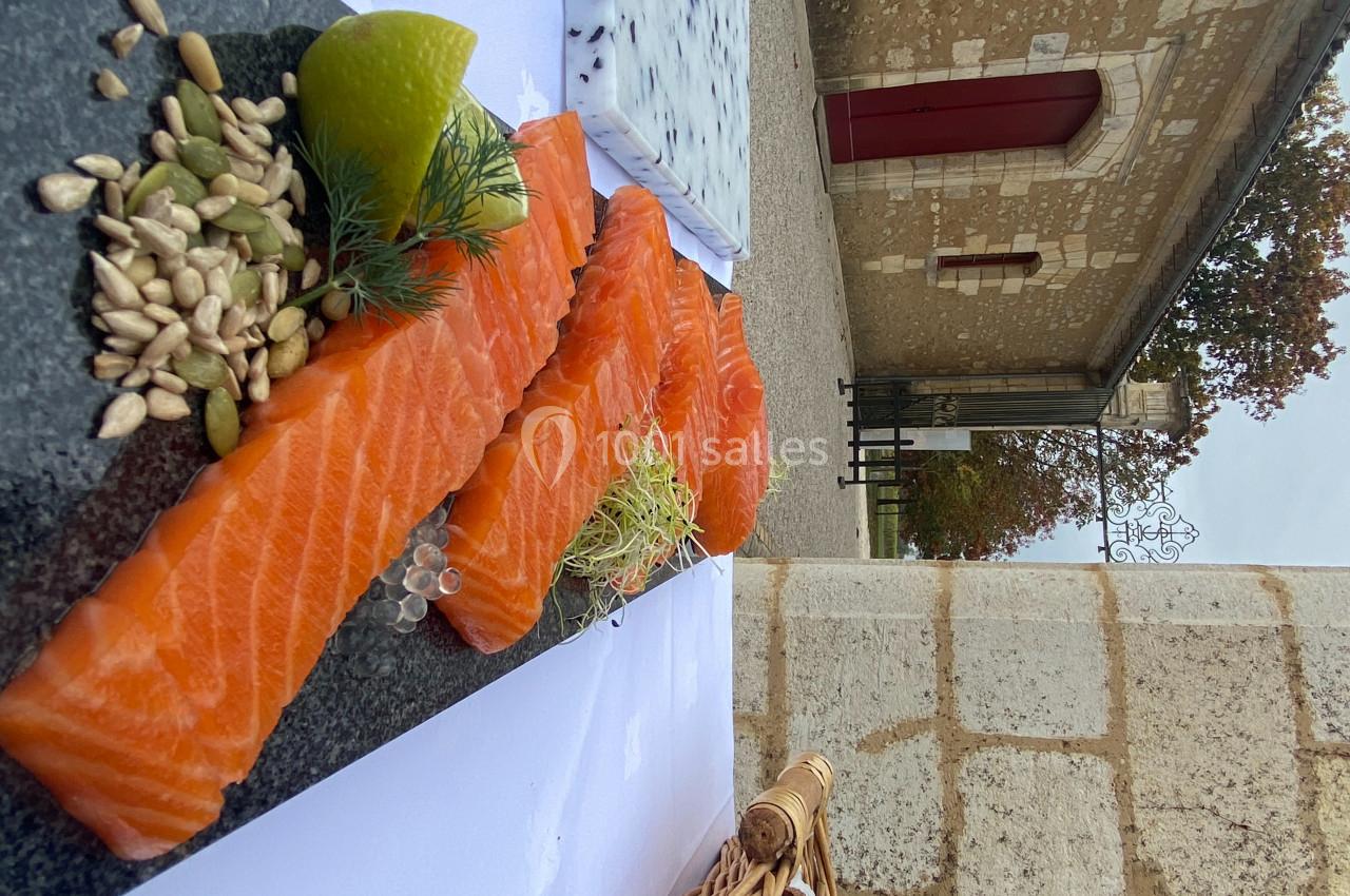 Tranches de saumon frais sur une ardoise avec graines, citron vert et herbes, en extérieur près d'un bâtiment en pierre.