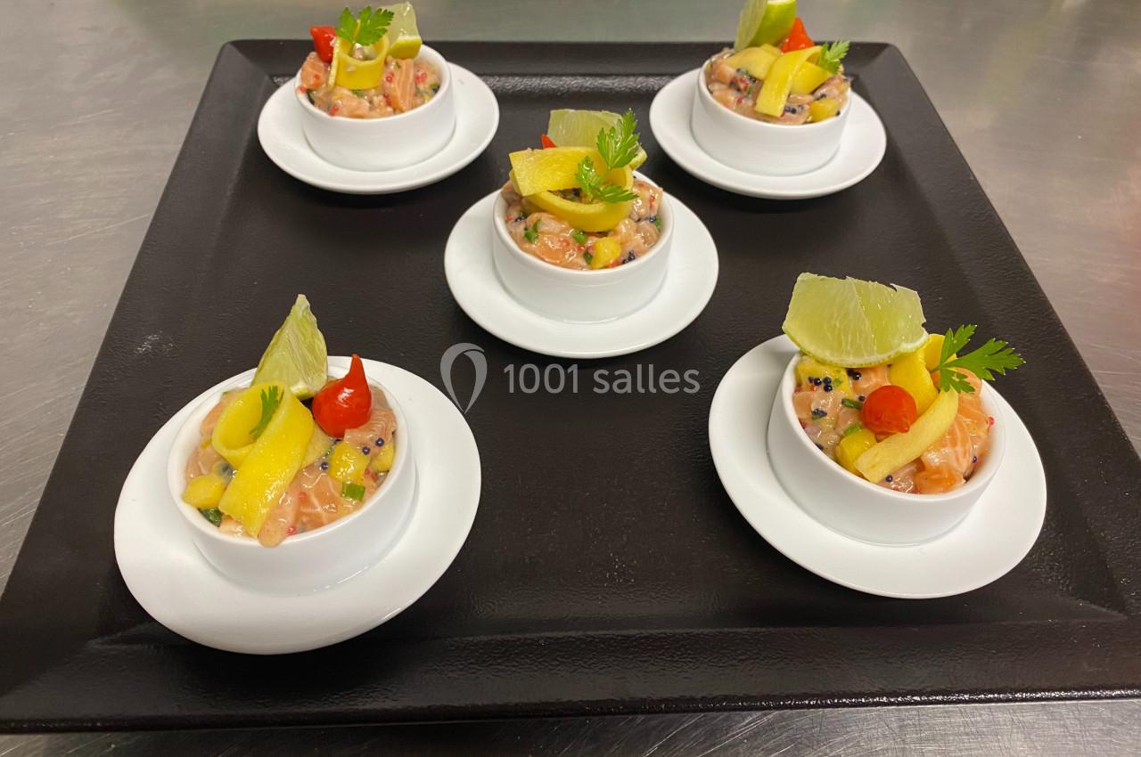 Cinq verrines de tartare de saumon garnies de citron, mangue et herbes, présentées sur un plateau noir.