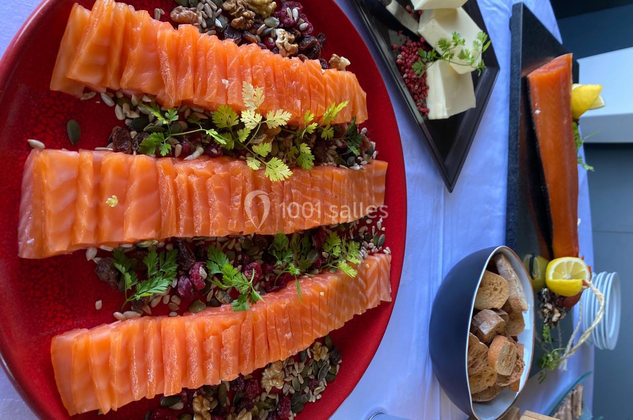 Assiette de saumon fumé tranché avec noix, graines et herbes, accompagnée de pain, fromage et citron sur une table.