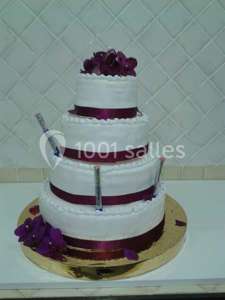 Gâteau de mariage à trois étages décoré de rubans bordeaux, fleurs violettes et détails argentés.
