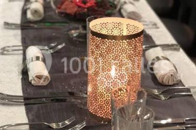 Table élégamment dressée avec bougies décoratives, serviettes pliées, verres en cristal et chemin de table sombre.