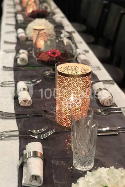 Table élégamment dressée avec bougies décoratives, serviettes pliées, verres en cristal et chemin de table sombre.