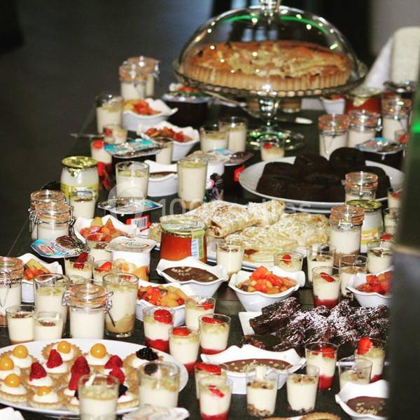 Table garnie de desserts variés, incluant verrines, fruits, pâtisseries et gâteaux sous une cloche en verre.