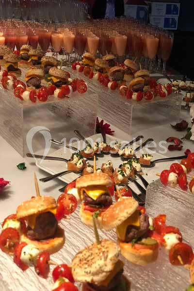Buffet avec mini-burgers, brochettes de tomates et mozzarella, verrines et autres amuse-bouches sur une table.