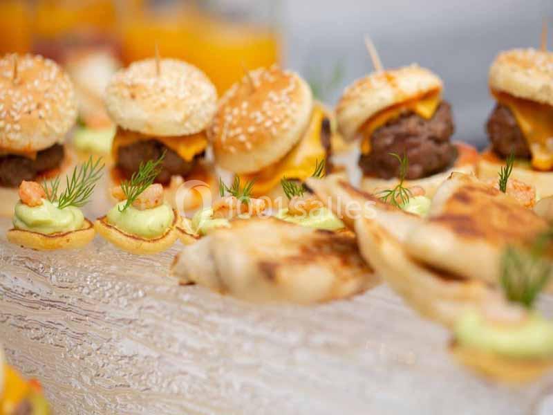 Assortiment de mini-burgers, canapés à l'avocat et brochettes sur une table en bois.