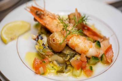Plat de viande grillée avec sauce et légumes dans une cocotte, présenté sur une planche en bois.