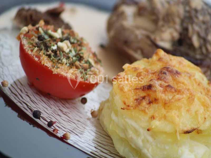 Tomate farcie aux herbes et gratin de pommes de terre servis sur une assiette avec une sauce en arrière-plan.