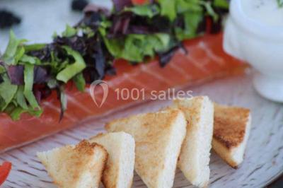Plat de viande grillée avec sauce et légumes dans une cocotte, présenté sur une planche en bois.
