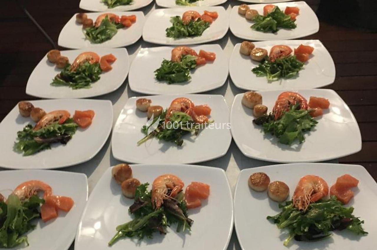 Assiettes dressées avec crevettes, noix de Saint-Jacques, saumon fumé et salade verte sur une table en bois.