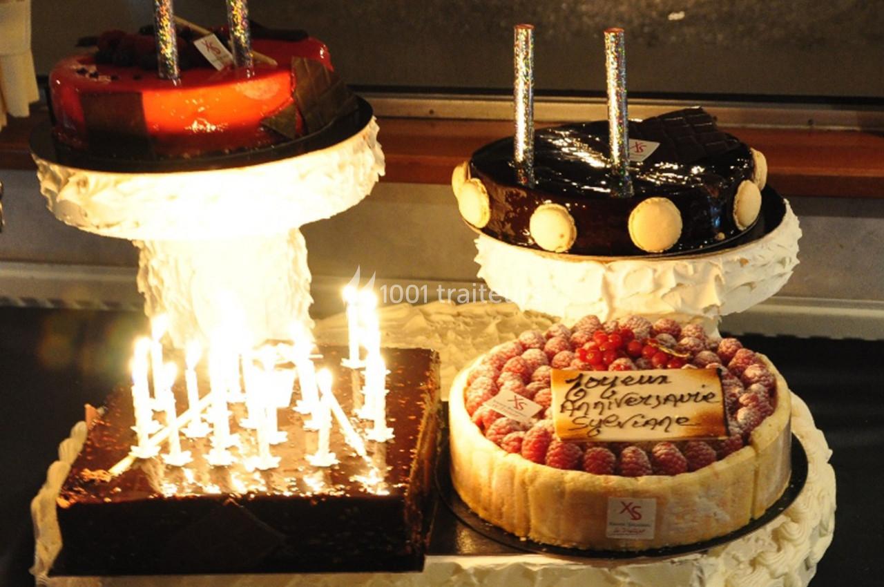 Quatre gâteaux d'anniversaire décorés, avec bougies allumées et un message écrit sur l'un d'eux.