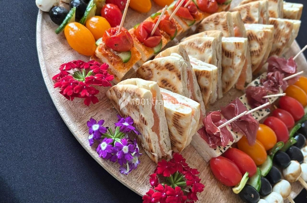 Plateau en bois garni de mini-sandwichs, brochettes de légumes, tomates cerises et fleurs décoratives.