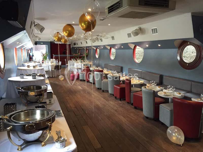 Salle de réception sur une péniche, décorée pour un événement avec tables dressées et ballons dorés.