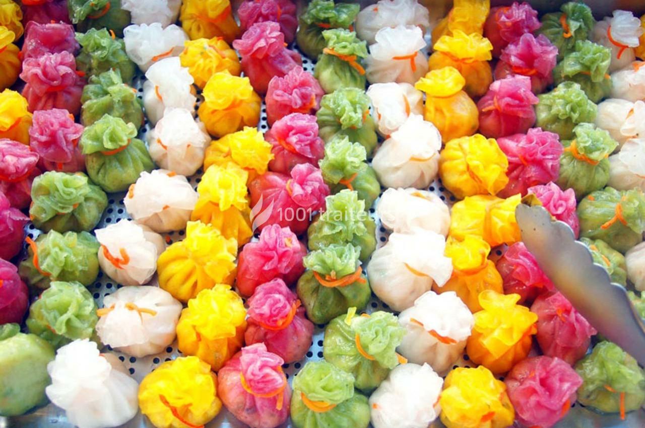 Assortiment de raviolis colorés à la vapeur disposés sur un plateau perforé.