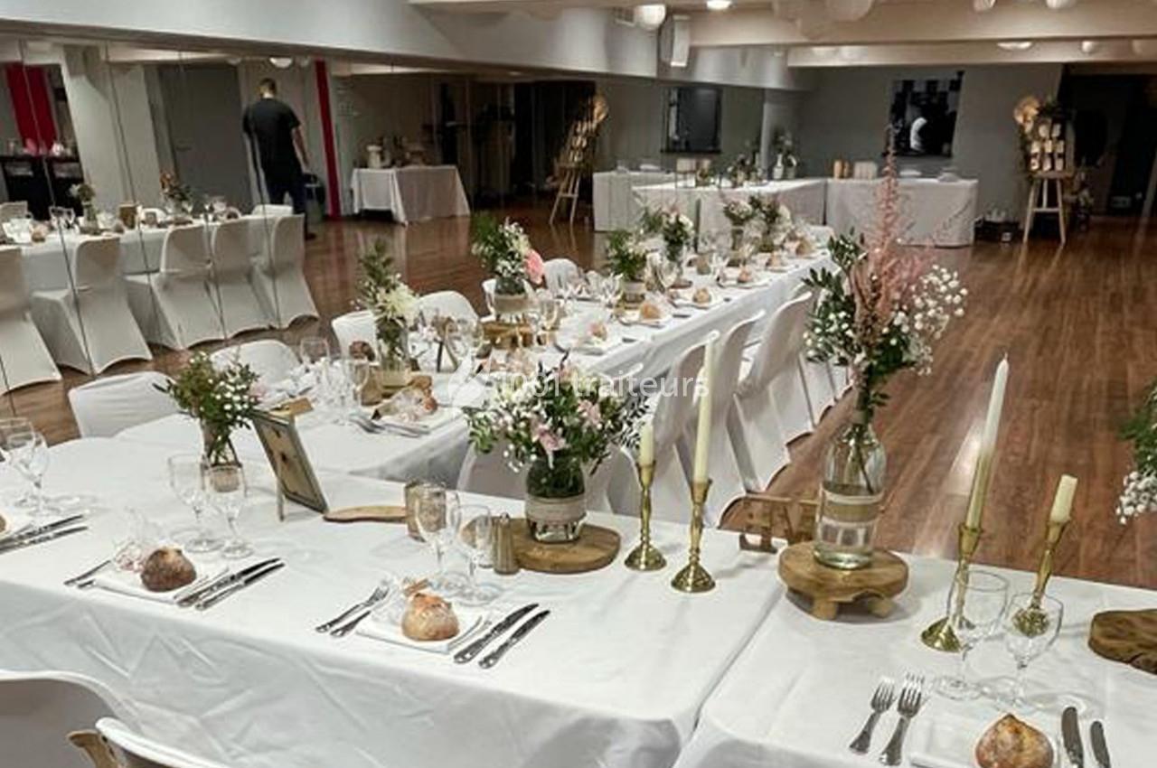 Salle décorée pour un événement avec des tables dressées, nappes blanches, bougies et arrangements floraux.