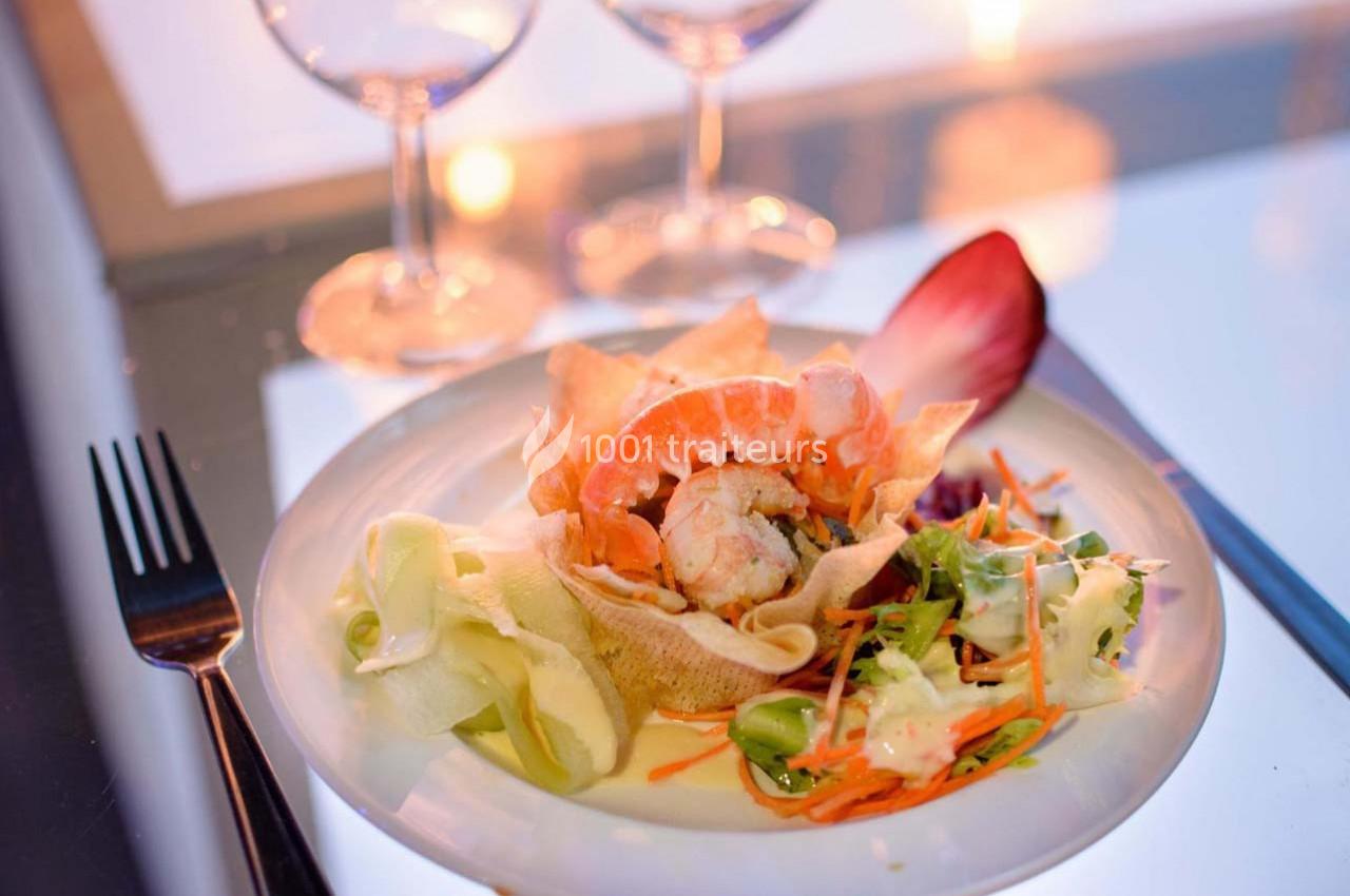 Assiette de crevettes avec légumes croquants, chips et sauce, servie sur une table élégamment dressée.