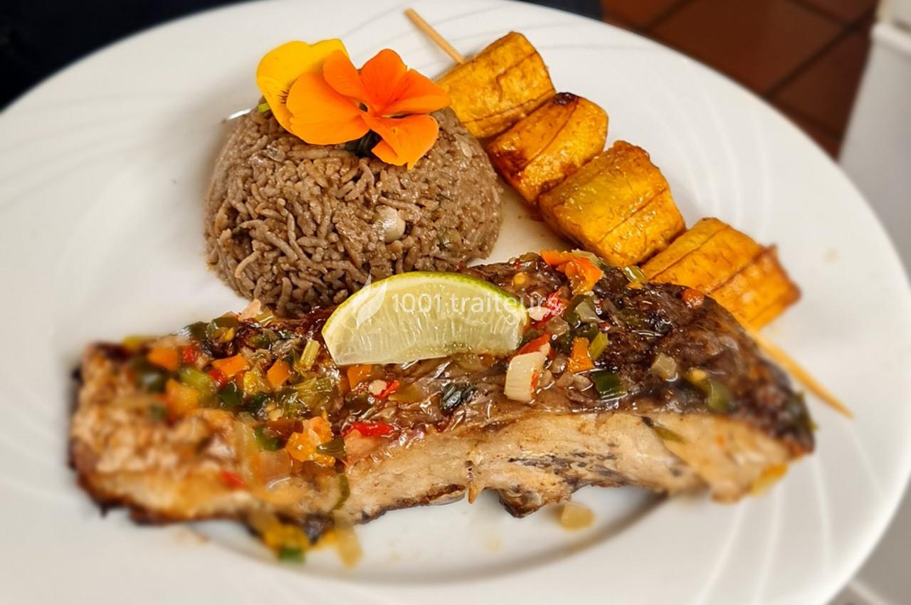 Assiette composée de poisson grillé avec sauce, riz, bananes plantains grillées et décoration florale.
