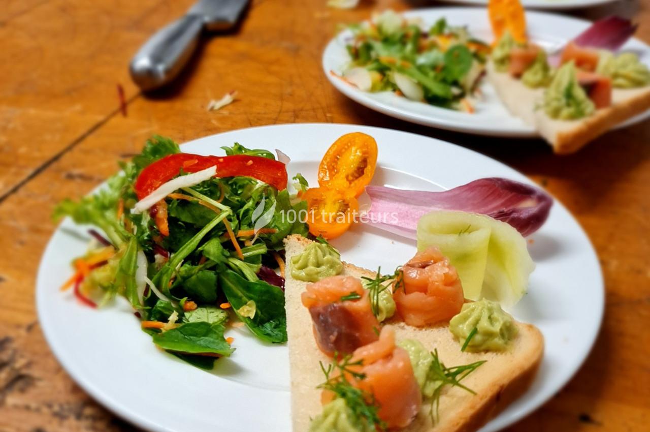 Assiette contenant une salade colorée et une tartine garnie de saumon, d'avocat et de légumes, sur une table en bois.