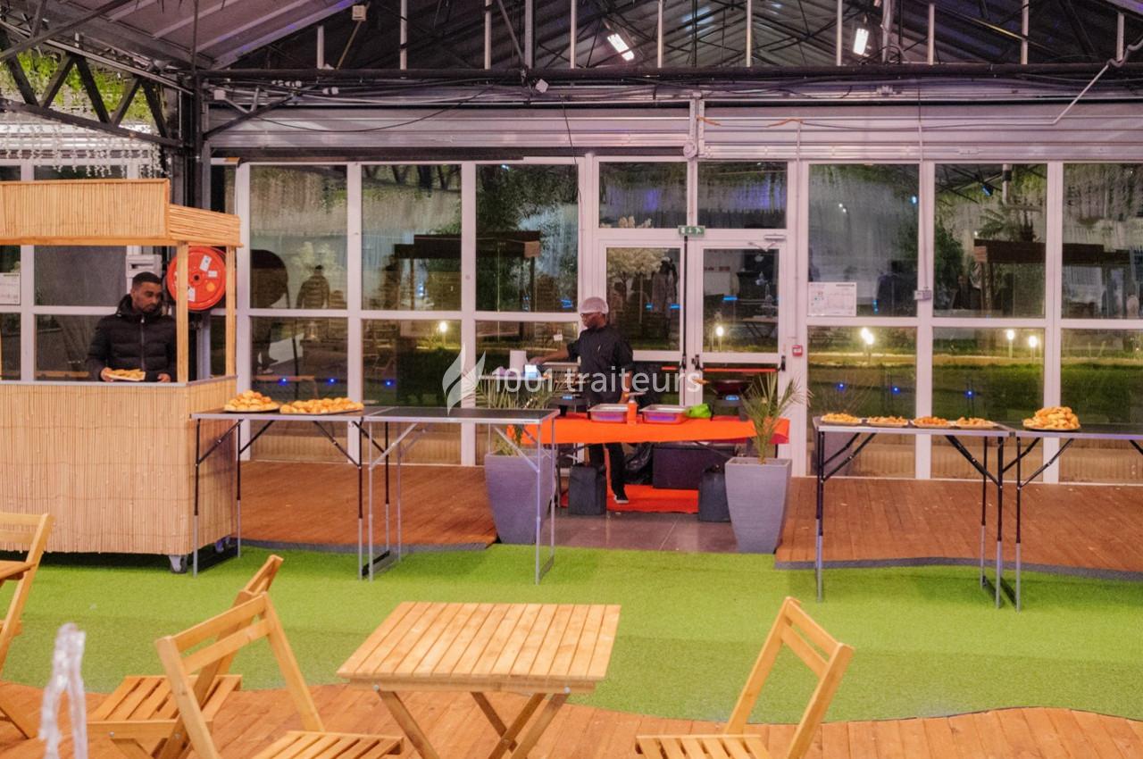 Un stand de restauration avec deux cuisiniers, des tables en bois et des plats disposés sur des tables dans un espace…