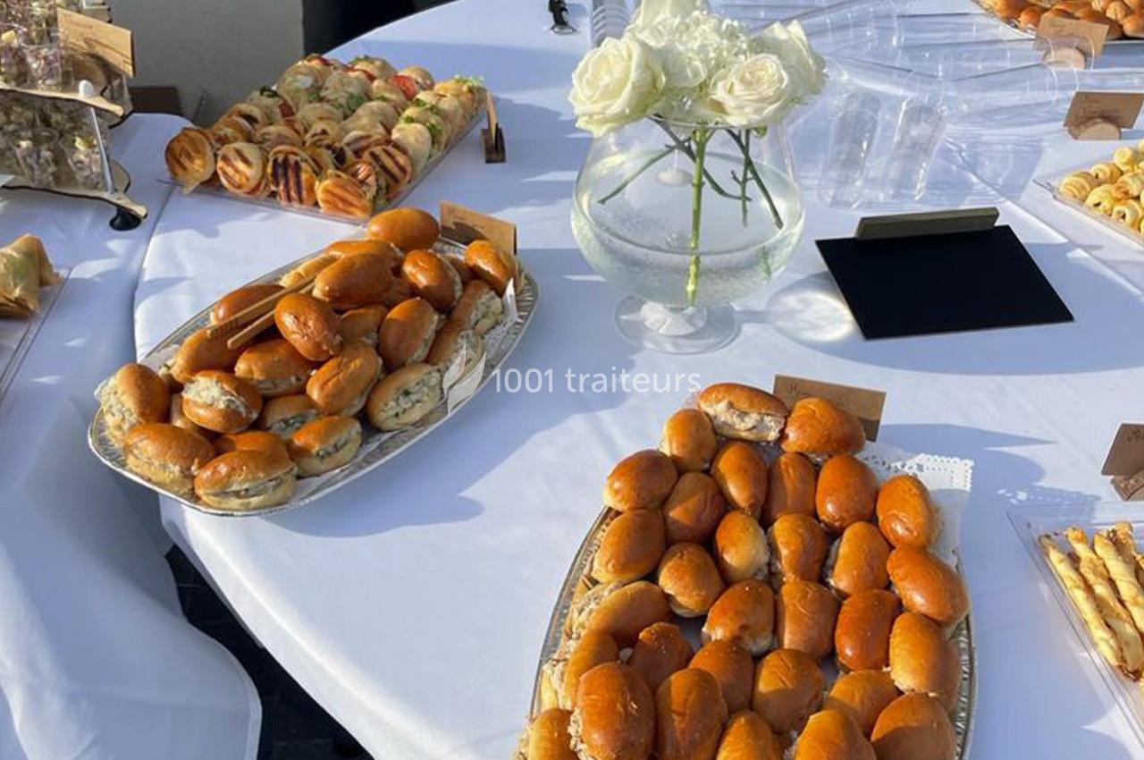 Plateaux de petits sandwichs et viennoiseries disposés sur une table blanche avec un vase de roses blanches.
