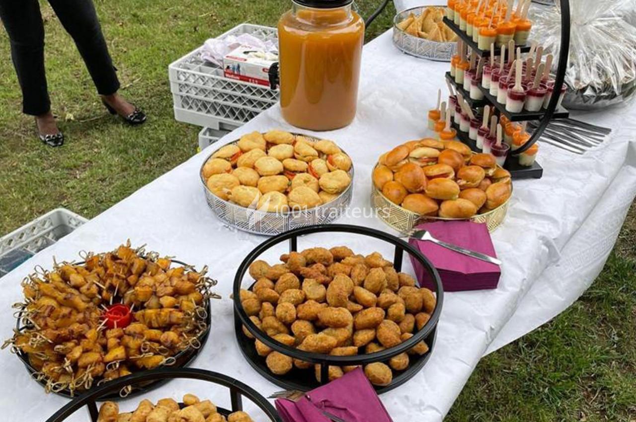 Buffet en plein air avec assortiments de bouchées salées, jus dans un grand bocal et verrines sur un présentoir.