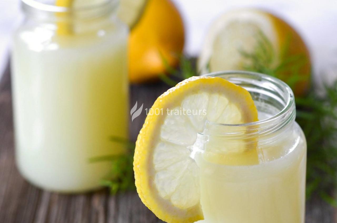 Deux verres de limonade avec des tranches de citron, posés sur une table en bois avec des citrons en arrière-plan.